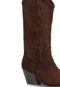 Bota de cowboy de ante marrón con costuras decorativas y un tacón apilado.