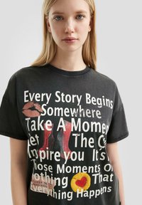 Schwarzes Baumwoll-T-Shirt mit einem grafischen Druck von roten High Heels, einem Lippenstiftabdruck und verschiedenen Textsprüchen in fett weißer Schrift.