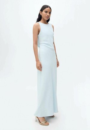 Robe sans manches bleu clair en tissu lisse, présentant une silhouette ajustée qui tombe jusqu'au sol. Associée à des talons dorés à lanières.