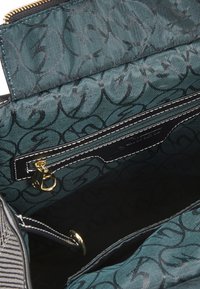 Interno di una borsa in tessuto verde a motivi, con una tasca con zip dotata di accessori in oro, bordo nero a contrasto e un audace design del logo.