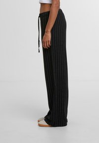Čierne široké nohavice s vertikálnymi bielymi prúžkami, elastickým pásom a detailom na šnúrku; mäkká tkanina a rovný strih.