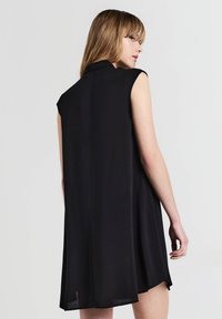 Abito nero senza maniche con colletto, texture liscia, taglio dritto e fessure laterali all'orlo, che mette in risalto un design minimalista.
