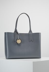 Szara skórzana torba tote o strukturalnym kształcie, długich uchwytach i okrągłej złotej metce. Posiada teksturowaną powierzchnię oraz minimalistyczny design.