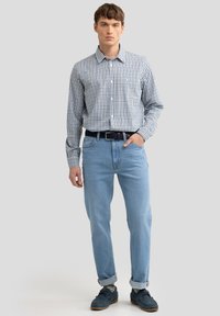 Geruit blauw-wit shirt, lichtblauwe spijkerbroek, donkere schoenen. Het shirt heeft lange mouwen en een kraag; de spijkerbroek is recht gesneden met omgeslagen zomen.