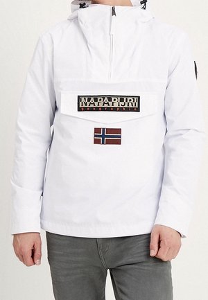 Osoba ubrana w białą kurtkę z kapturem i przednim zamkiem, z naszywką Napapijri i naszywką z flagą Norwegii, w połączeniu z szarymi spodniami.