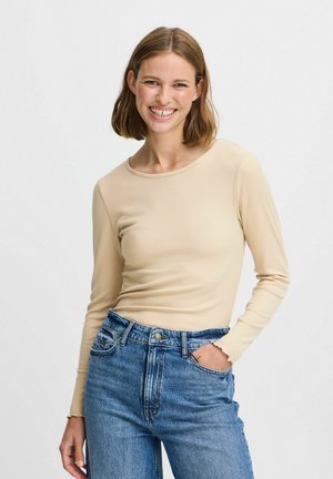 Top de manga larga acanalado en beige, combinado con jeans de mezclilla azul de cintura alta con dobladillo deshilachado y diseño clásico de cinco bolsillos.