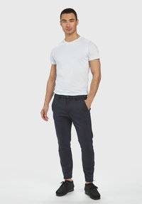 Weißes Crew-Neck T-Shirt, schmal geschnittene marineblaue Hose mit Taschen und schwarze Schnürschuhe. Das glatte Material und das maßgeschneiderte Design sorgen für einen modernen Look.