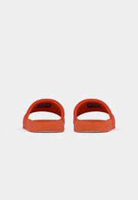 Paire de sandales compensées orange vues de face sur un fond gris clair uni.