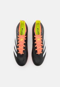 Botas de fútbol negras con material sintético texturizado, cordones naranja brillante y franjas blancas notables; el interior cuenta con acolchado verde.