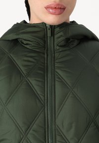 Grüne gequiltete Pufferjacke mit Reißverschluss und Kapuze. Verfügt über eine glatte, glänzende Textur und eine rhombenartige Steppnaht.