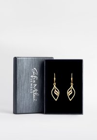 Orecchini a forma di foglia d'oro con un design ondulato, caratterizzati da accenti luccicanti, esposti in una scatola foderata in velluto nero. La scatola ha una superficie testurizzata.