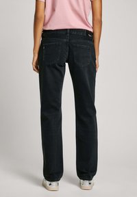 Vaqueros de mezclilla negra con un corte relajado, diseño de cinco bolsillos, costuras sutiles y una textura suave; combinados con una camiseta rosa claro.