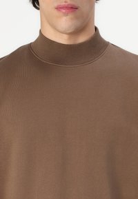 Brown high-collar pullover made of soft fabric. Features a smooth texture with a fitted design, visible stitching along the collar.