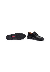 Chaussures de ville en cuir noir avec une surface lisse, une couture détaillée, un bout rond, et une semelle en caoutchouc texturée avec une accent rouge.