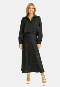 Czarna długa sukienka z kołnierzykiem, zapinana na guziki, z długimi rękawami. Posiada rozsiane białe kropki i gładką, zwiewną spódnicę.