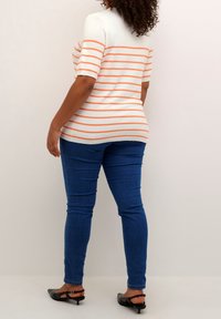 Striped short-sleeve top in white and orange, paired with blue skinny jeans. The top has a round neck and a fitted silhouette. Black heels.