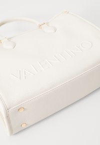 Borsa a mano in pelle bianca dal tessuto texturizzato con logo "VALENTINO" impresso, hardware in tono oro e manici arrotondati. Presenta piedi metallici protettivi.