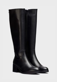 Botas de cuero negro hasta la rodilla con tacón cuadrado, que cuentan con una cremallera lateral y una textura suave y mate. Forma angular con puntas redondeadas.