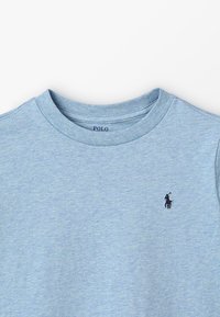 Ljusblå bomullströja med rund hals, korta ärmar och en liten marinblå logga på vänster bröst. Mjuk känsla och avslappnad passform.