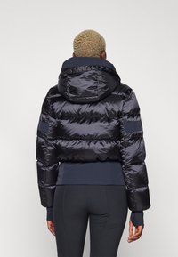 Zwarte pufferjack met een capuchon, voorzien van een glanzende, gewatteerde textuur, elastische manchetten en een aansluitend ontwerp bij de taille. Glad stoffen afwerking.