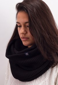 Black knitted infinity scarf with a ribbed texture and a small logo tag. Soft, thick fabric wrapped around the neck.