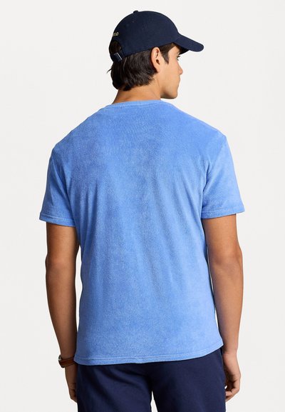 Tricou bleu deschis, cu mânecă scurtă, fabricat dintr-un material texturat; vedere din spate care arată un gât rotund standard și mâneci ușor răsucite.