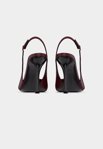 Par rdečih visokih pet z zanko na hrbtni strani in tankimi petami stileto, videnih od zadaj na beli podlagi.