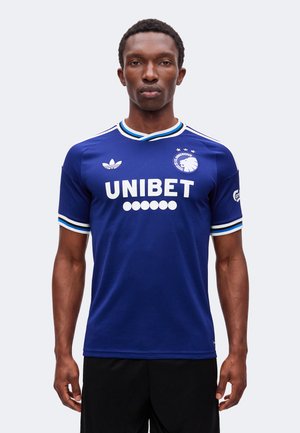 Mand stående frontalt iført en blå FC København fodboldtrøje med UNIBET sponsor og Adidas logo.