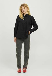 Camicia di cotone nera con chiusura a bottoni, maniche lunghe e vestibilità rilassata, abbinata a jeans grigi sbiaditi e scarpe rosse con lacci.