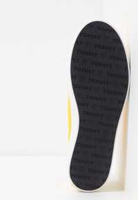 Żółty tenisówka z białą podeszwą środkową. Czarna gumowa podeszwa zewnętrzna z wytłoczonym napisem "TOMMY" oraz wzorem serc. Gładka tekstura, okrągły kształt noska.