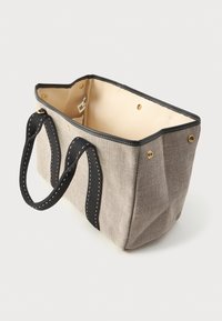 Καμβαδέ σακίδιο με μπεζ εξωτερικό, μαύρες λαβές και εσωτερικό. Διαθέτει χρυσές εσωτερικές ακίδες και λευκές ραφές κατά μήκος των ραφών.