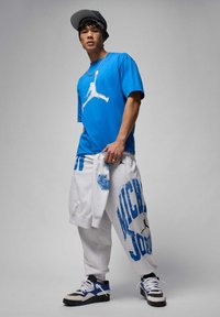 Blaues Grafik-T-Shirt mit weißem Jumpman-Logo, kombiniert mit grauen Jogginghosen mit blauem "MICHAEL JORDAN"-Schriftzug und Akzenten sowie schwarzen und blauen Sneakers.
