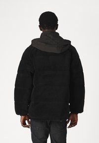 Czarna polarowa kurtka z kapturem, o pluszowej fakturze i prostym kroju. Tył ma poziome szwy oraz elastyczne mankiety.