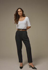 Bijela majica s izrezom u obliku kruške, u kombinaciji s crnim hlačama visokog struka s nabranim detaljima, zategnutim smeškanim remenom i crnim cipelama s oštrom špicom.