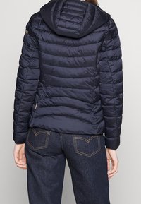 Marineblå fyldjakke med horisontal quiltet design, fastgjort hætte og sidelommer. Teksturstof og letvægtsisolering.