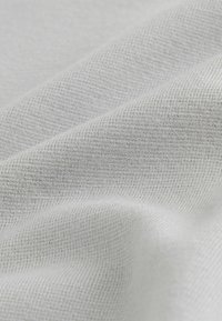 Svetlosivá tkanina s textúrovaným, tkaným vzorom. Povrch vyzerá mäkko, so subtílnymi farebnými odtieňmi a jemným leskom.