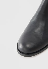Czarny skórzany botek za kostkę z zaokrąglonym noskiem, gładką fakturą i subtelnym przeszyciem. Gumowa podeszwa z teksturowanym brzegiem.