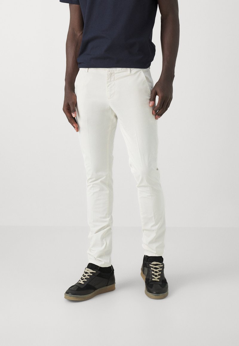 Pantaloni slim-fit bianchi realizzati in tessuto misto cotone, con design a cinque tasche, zip frontale, abbinati a sneakers nere con lacci beige.