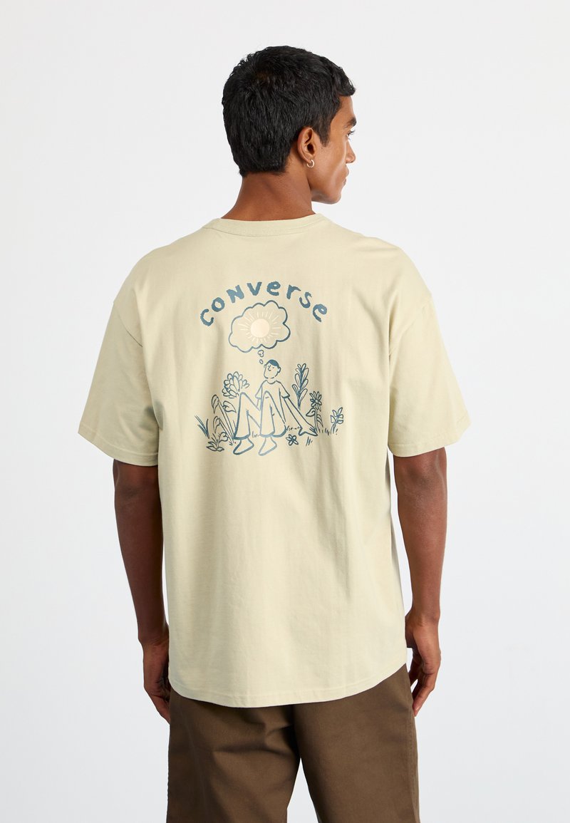 Cream-colored cotton t-shirt featuring a graphic design of a figure and flora on the back. Short sleeves, relaxed fit, and round neck.