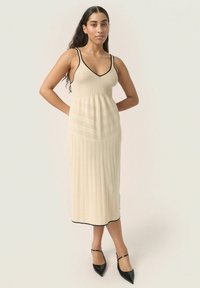 Abito midi a maglia beige con motivo a costine, rifiniture nere al colletto e all'orlo, e busto aderente che si allarga in vita.