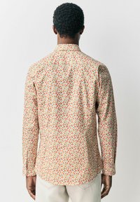 Camisa de manga larga con fondo beige y un patrón de hojas multicolores. Ajuste slim, cuello abotonado y puños con un solo botón.