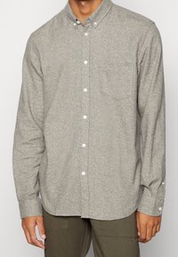 Graues Hemd aus strukturiertem Stoff, mit Kragen, Brusttasche und weißen Knöpfen, langen Ärmeln und abgerundetem Saum.