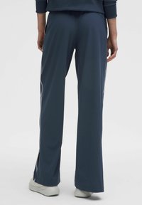 Tamno plave atletske hlače s bočnim prorezima i bijelim detaljima, s opuštenim krojem i glatkom teksturom tkanine.