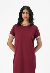 Burgundin t-paita mekko lyhyillä hihoilla, jossa on harmaat käänteet. Pehmeä kangas, rento malli ja sivutaskut. Yksinkertainen muotoilu.