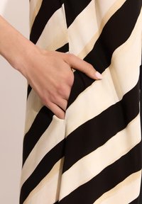 Dzięki gładkiej teksturze tkaniny w czarno-brązowe paski, widoczny jest praktyczny detal projektu – ręka wsunięta w boczną kieszeń.