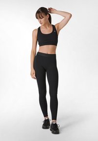 Musta urheiluliivi, jossa on teksturoitu nauha, jossa lukee "Goddess", ja siihen sopivat mustat legginsit. Materiaali näyttää olevan joustavaa ja vartalonmyötäistä.
