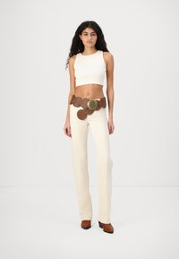 Crème crop top en wijde broek met een gedetailleerde bruine leren riem met ronde uitsparingen en een grote messing gesp.