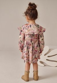Květinové šaty v růžové barvě s dlouhými rukávy, volánovým límečkem a elastickými manžetami. Doplněné koženými kotníkovými botami světle hnědé barvy s dekorativním prošitím.
