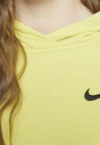 Felpa gialla brillante con cappuccio regolabile, caratterizzata da un logo Nike nero sul petto. Materiale in cotone liscio con una morbida texture.