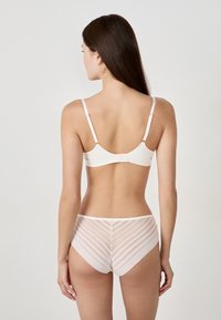 Soutien-gorge beige clair avec des bretelles fines, une finition lisse, et une culotte taille haute assortie dotée de panneaux rayés transparents à l'arrière.